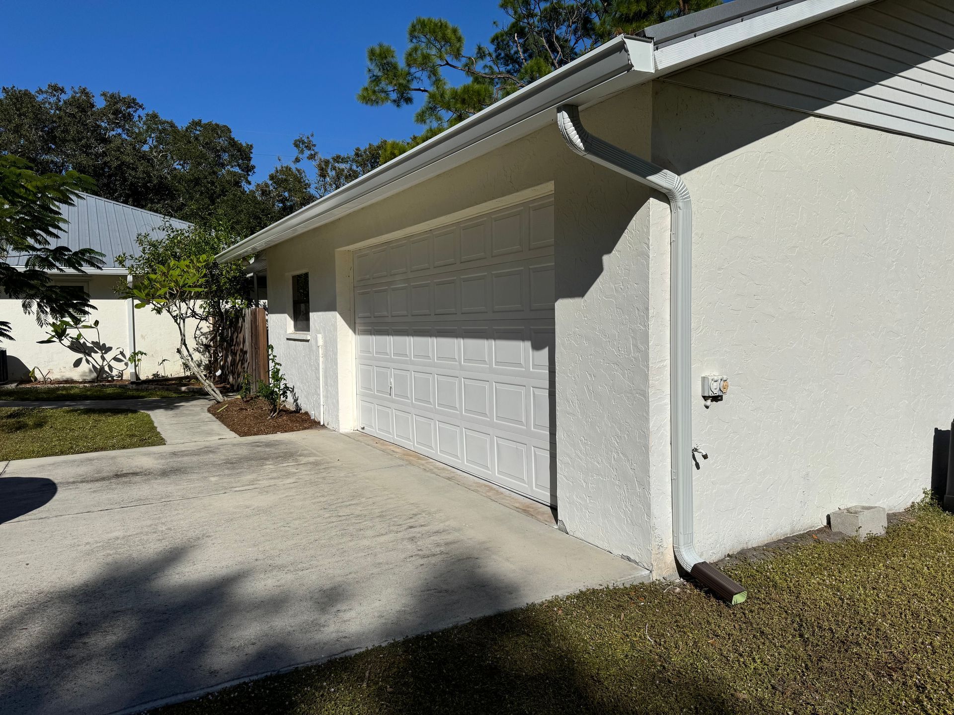 White stucco garage with white garage door, concrete driveway, and white gutter system.