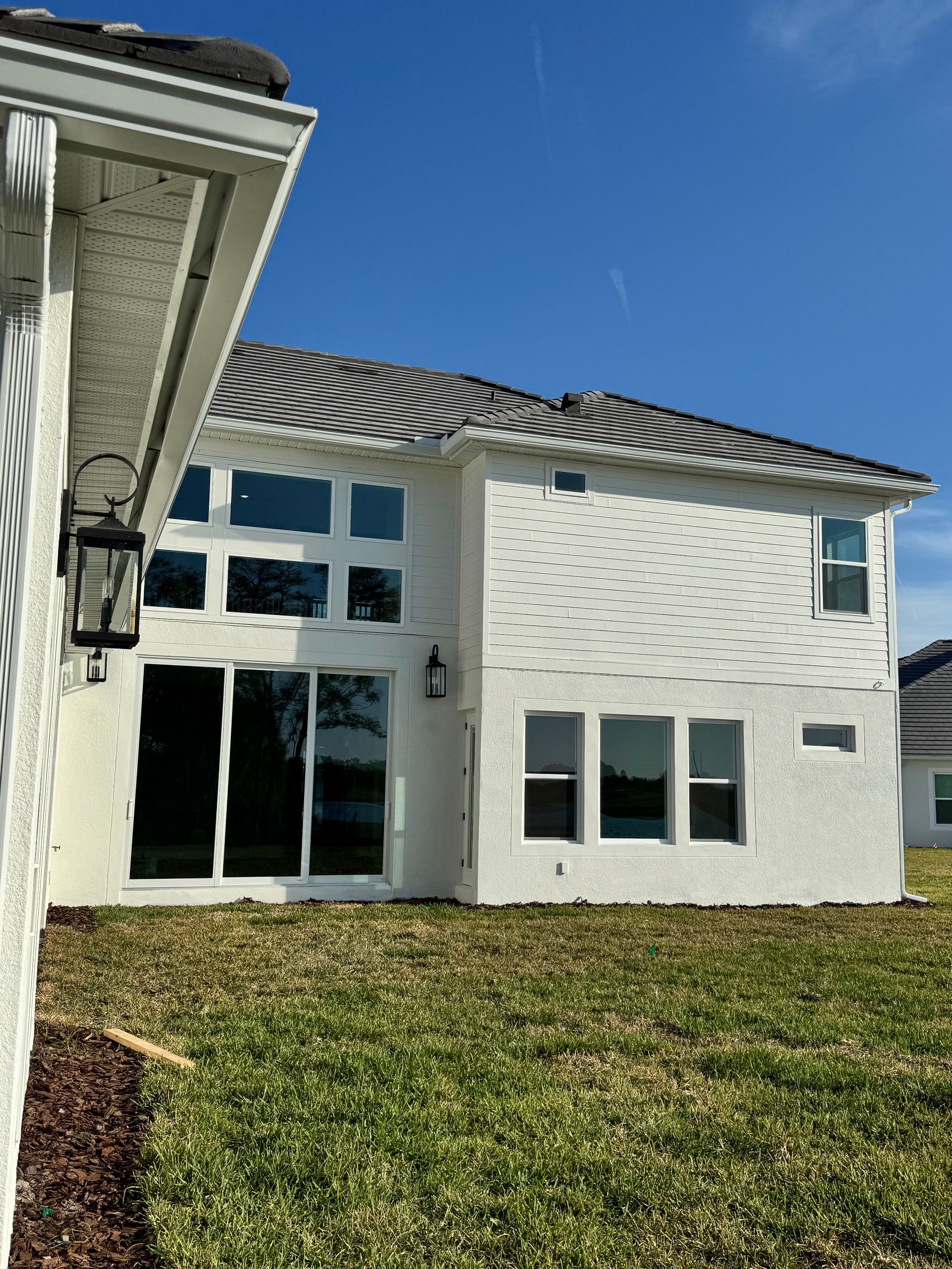 White stucco house with dark roof, windows, and grass lawn against a blue sky.
