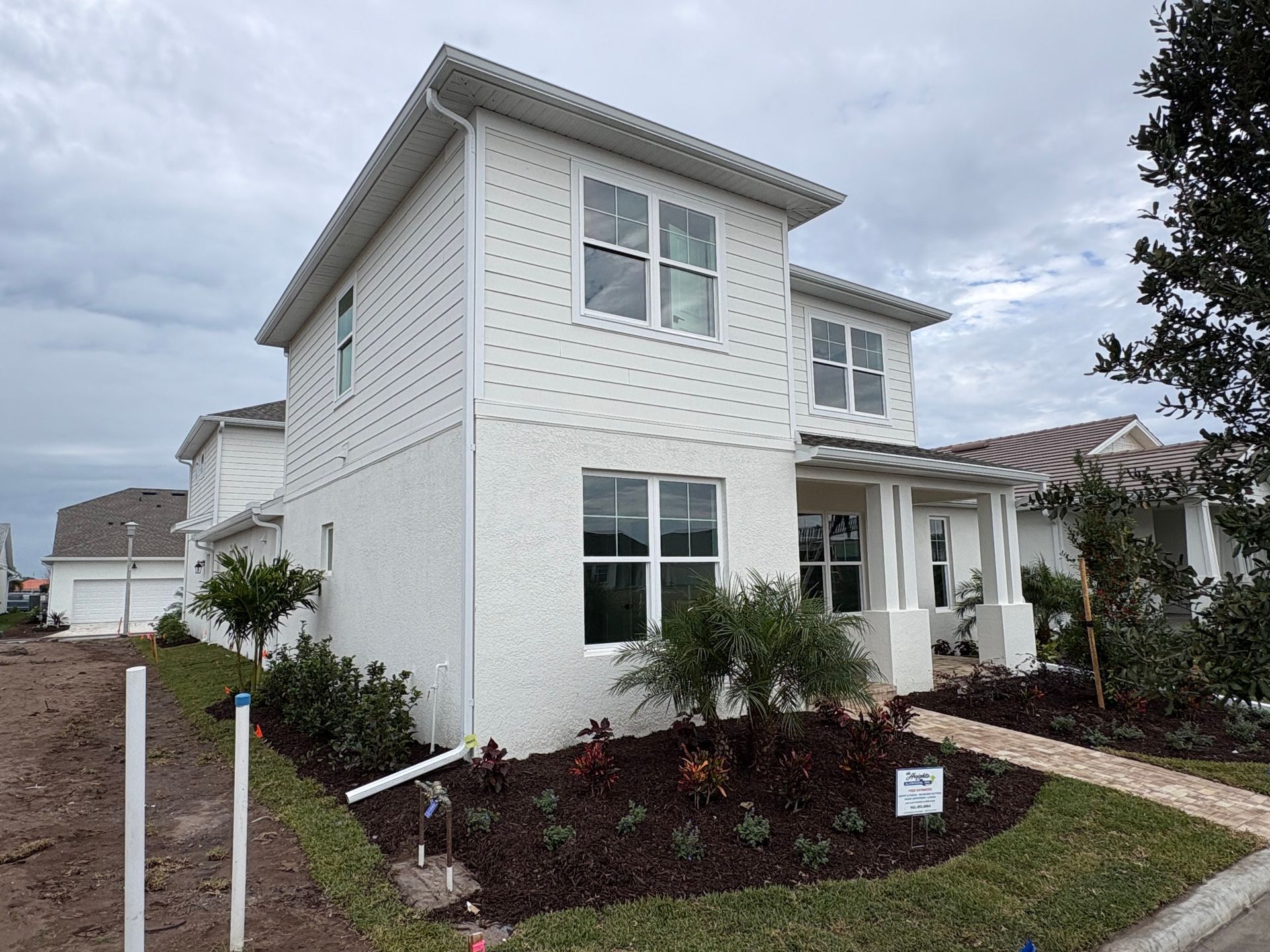 Two-story white house with light grey roof, landscaping, and a cloudy sky.