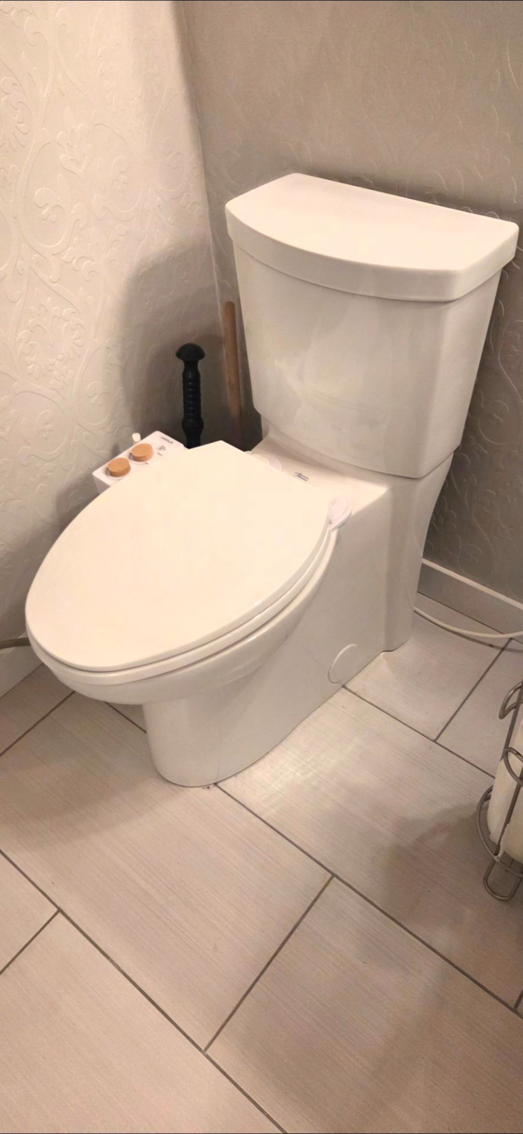 White toilet in a tiled bathroom corner with a closed lid and toilet paper nearby