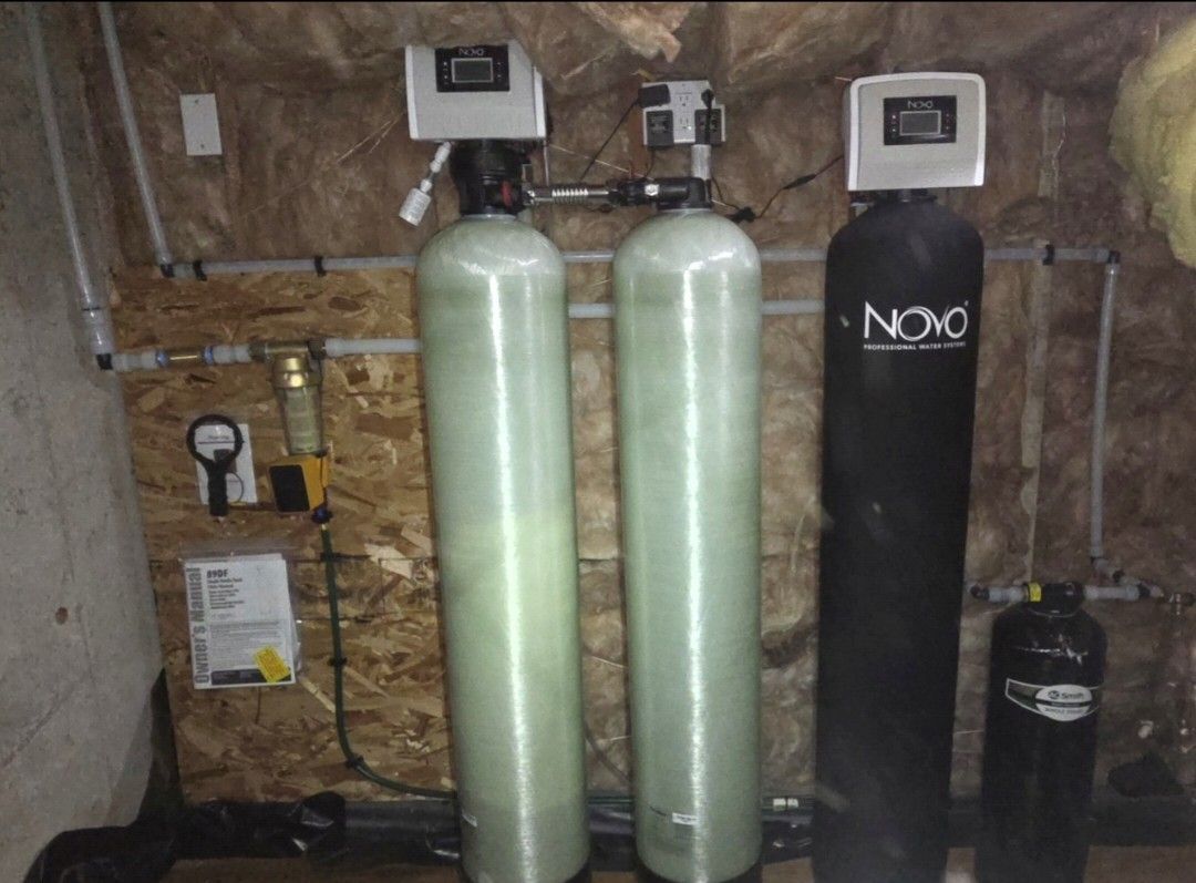 Water treatment equipment with two tall green tanks and a black NOC unit in a utility room