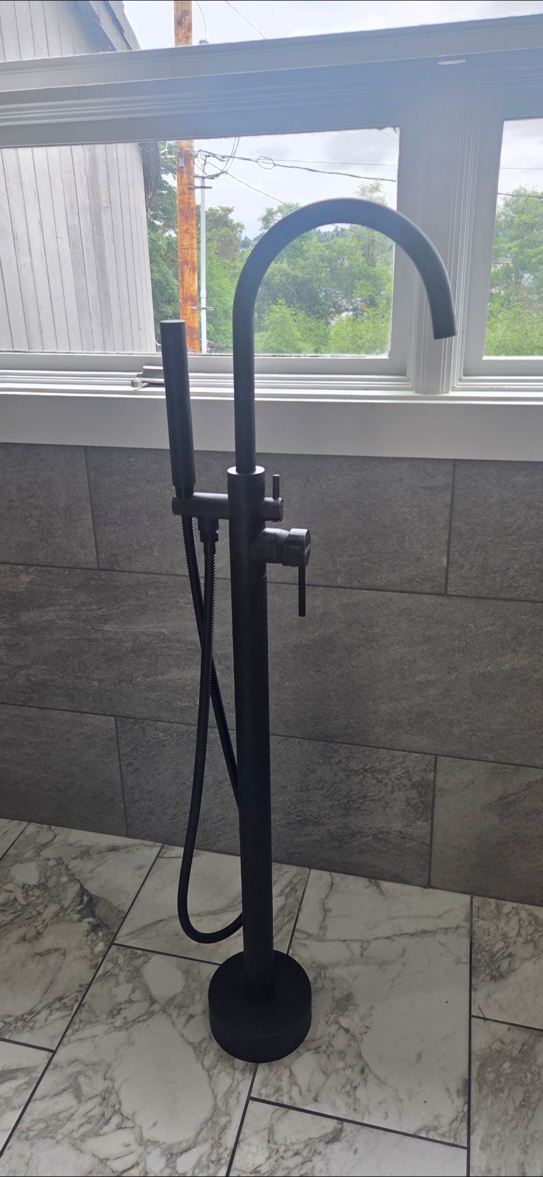 Black manual water pump with hose on a concrete floor by a windowed wall.