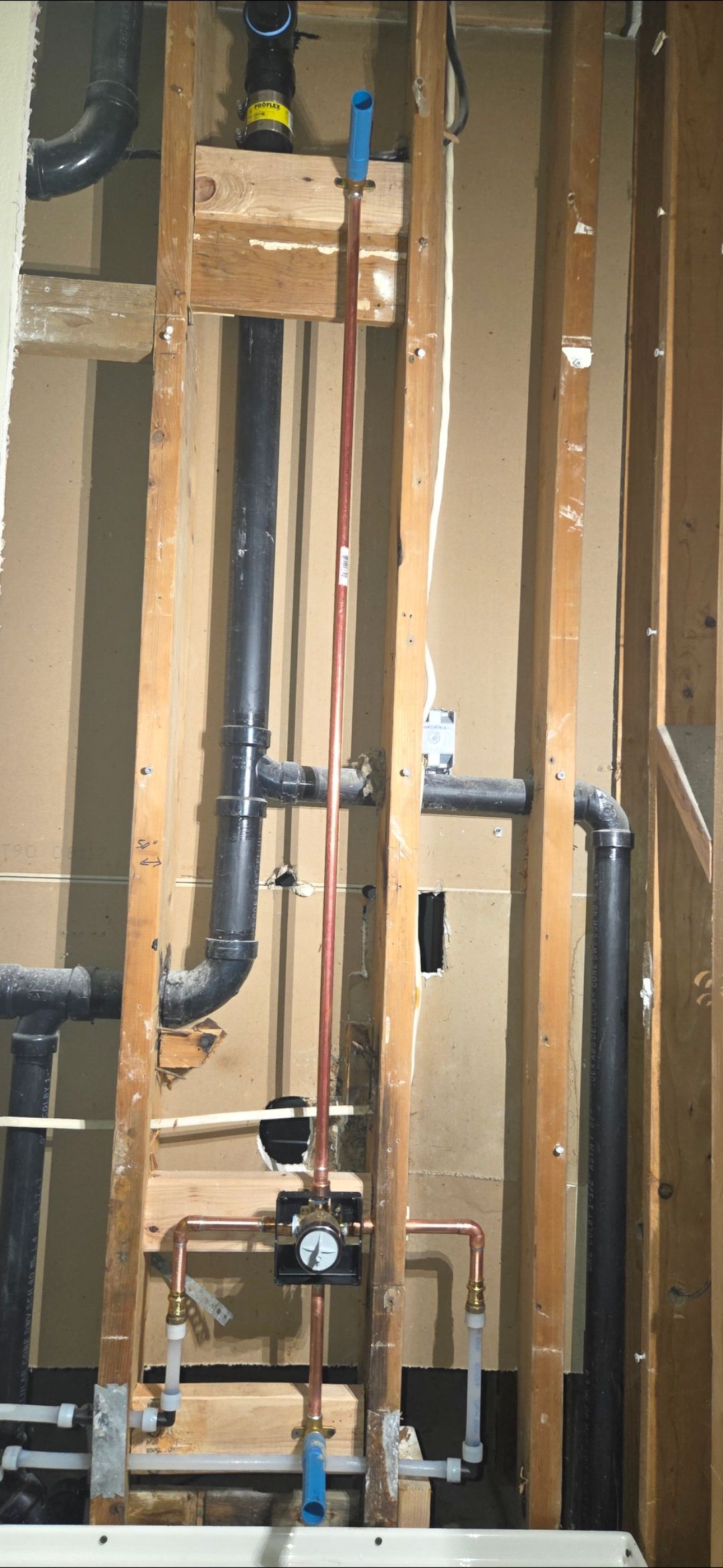 Exposed wall plumbing with copper pipes, PVC drains, and a utility meter in an unfinished space