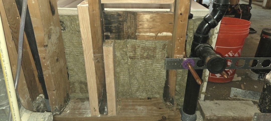 Exposed wall framing with pipes, insulation, and a black valve in an unfinished utility space