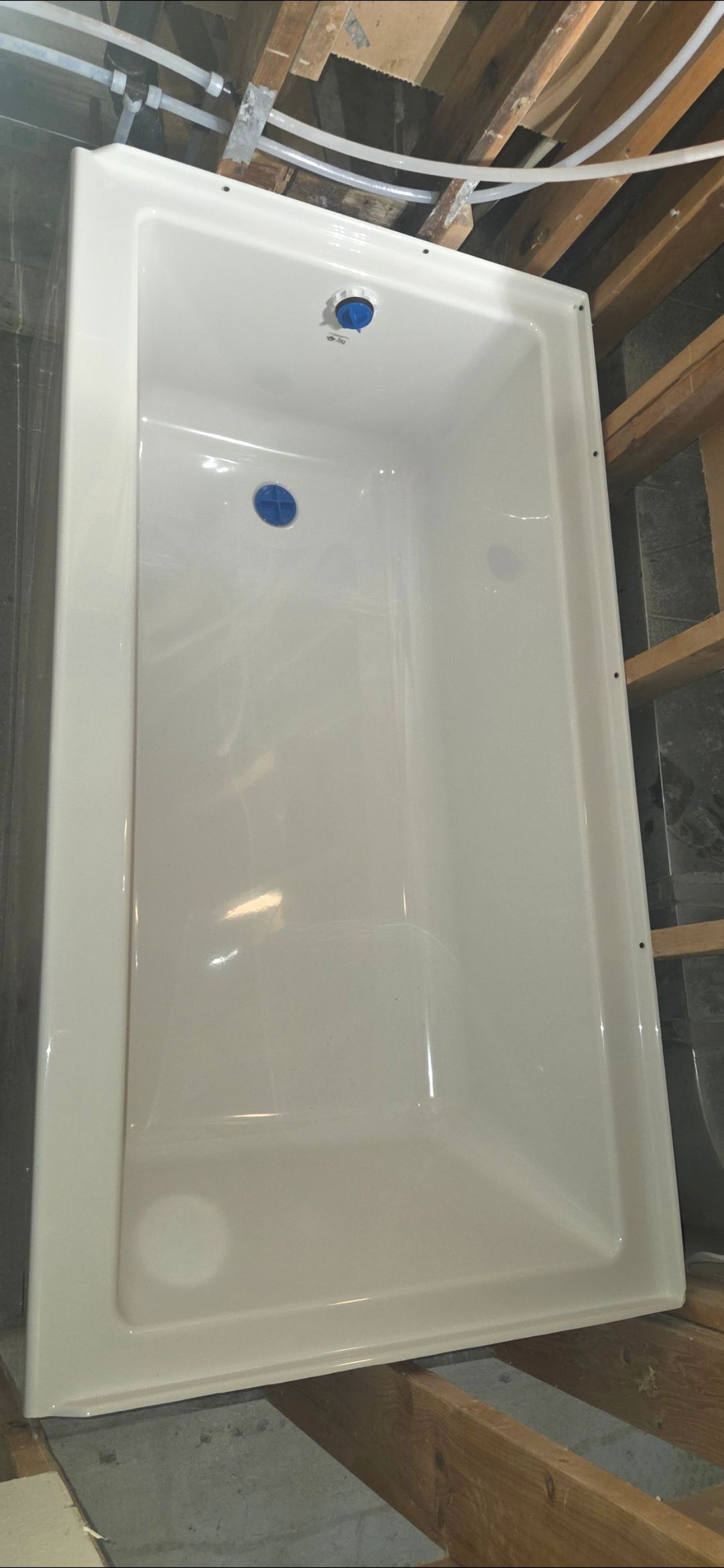 White rectangular bathtub or shower base in a construction setting with exposed framing and pipes