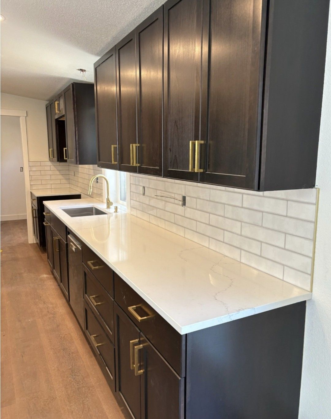 Modern galley kitchen with dark cabinets, white countertops, and white subway tile backsplash