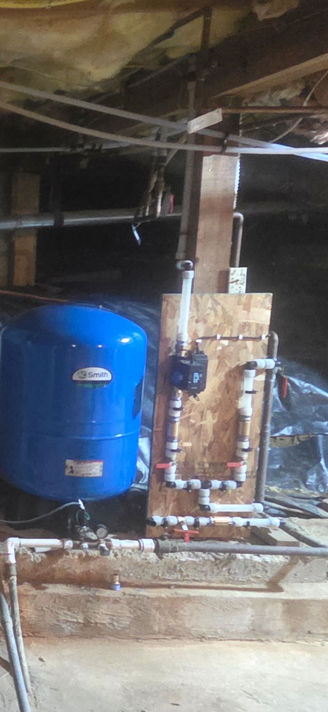 Blue pressure tank and copper piping in a dim basement utility area with exposed beams.