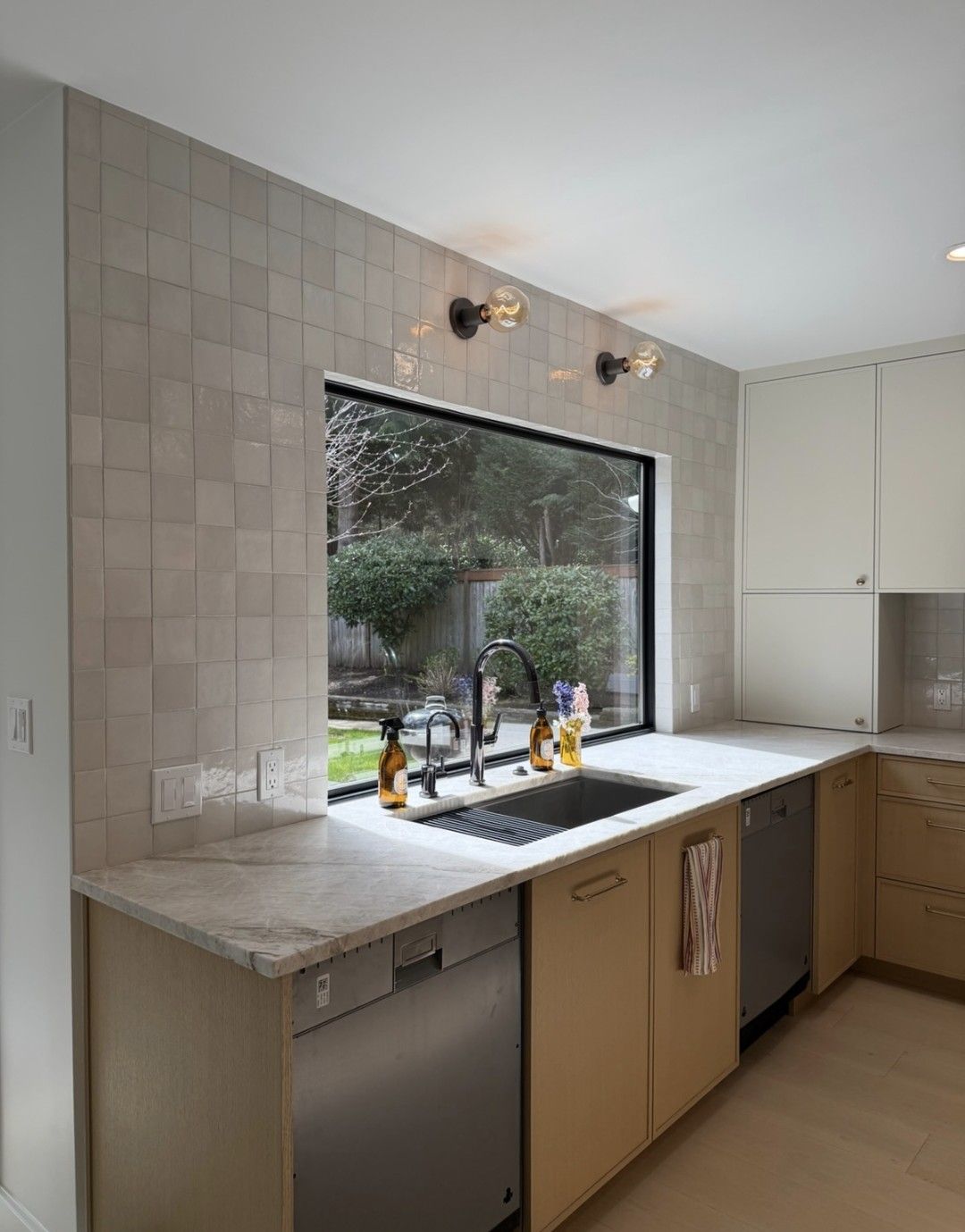 Modern kitchen with a large window over a sink, light wood cabinets, and a tiled backsplash.