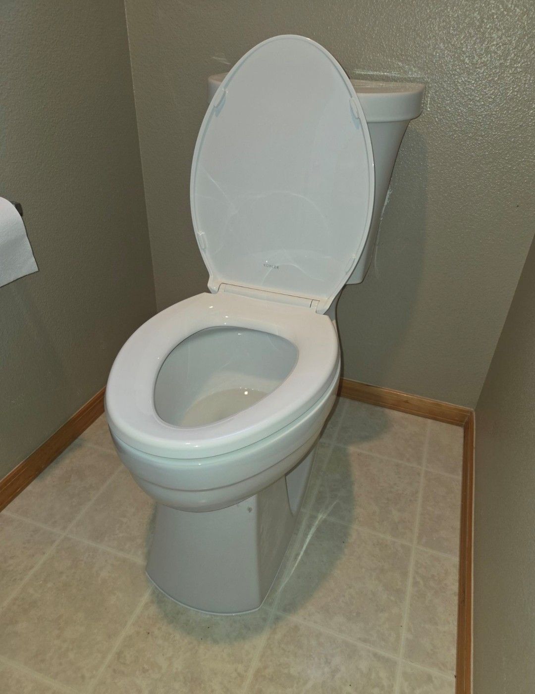 White toilet with lid up in a small bathroom with beige tile floor and green walls