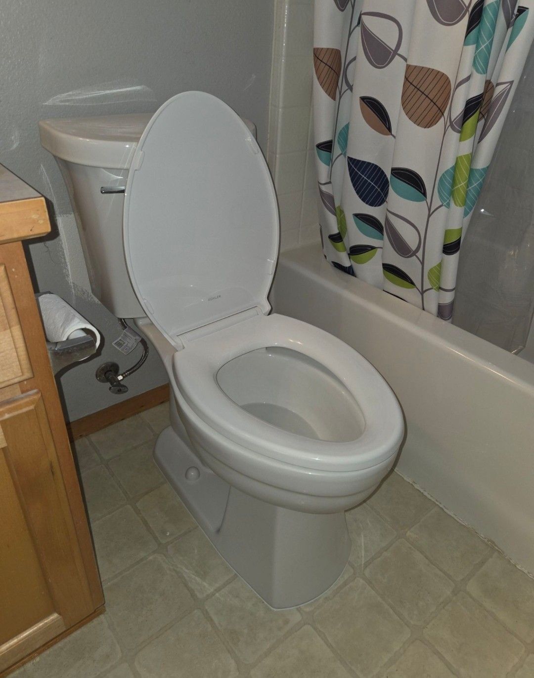 White toilet in a small bathroom with bathtub, shower curtain, and sink cabinet nearby.