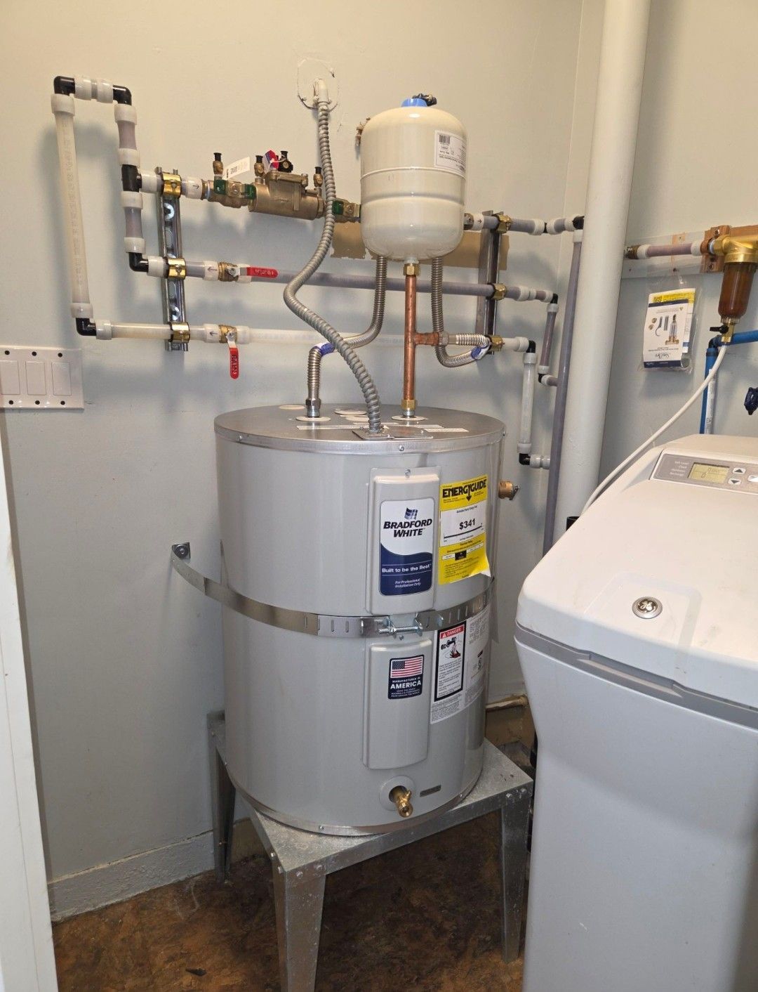 Water heater and plumbing in a utility room beside a white appliance.