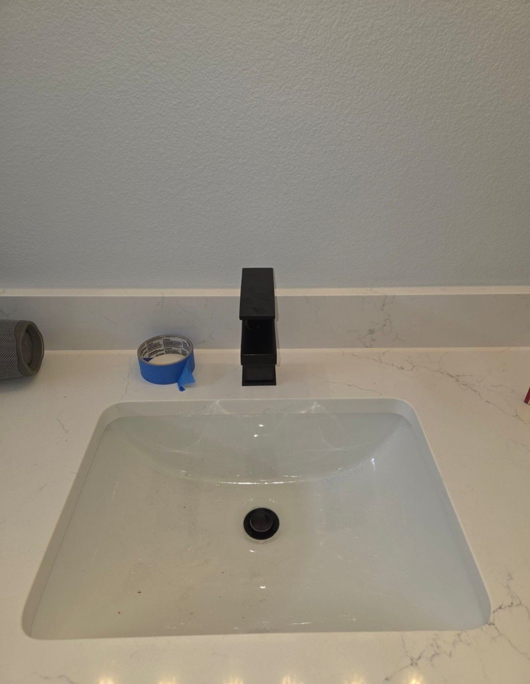 Bathroom sink with a black faucet and a small blue tape roll on the counter.
