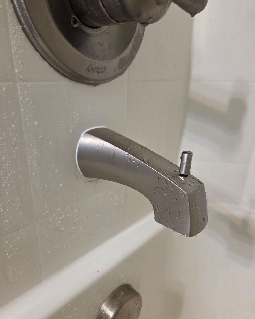 Silver bathtub faucet spout with a small upward pin in a tiled bathroom.