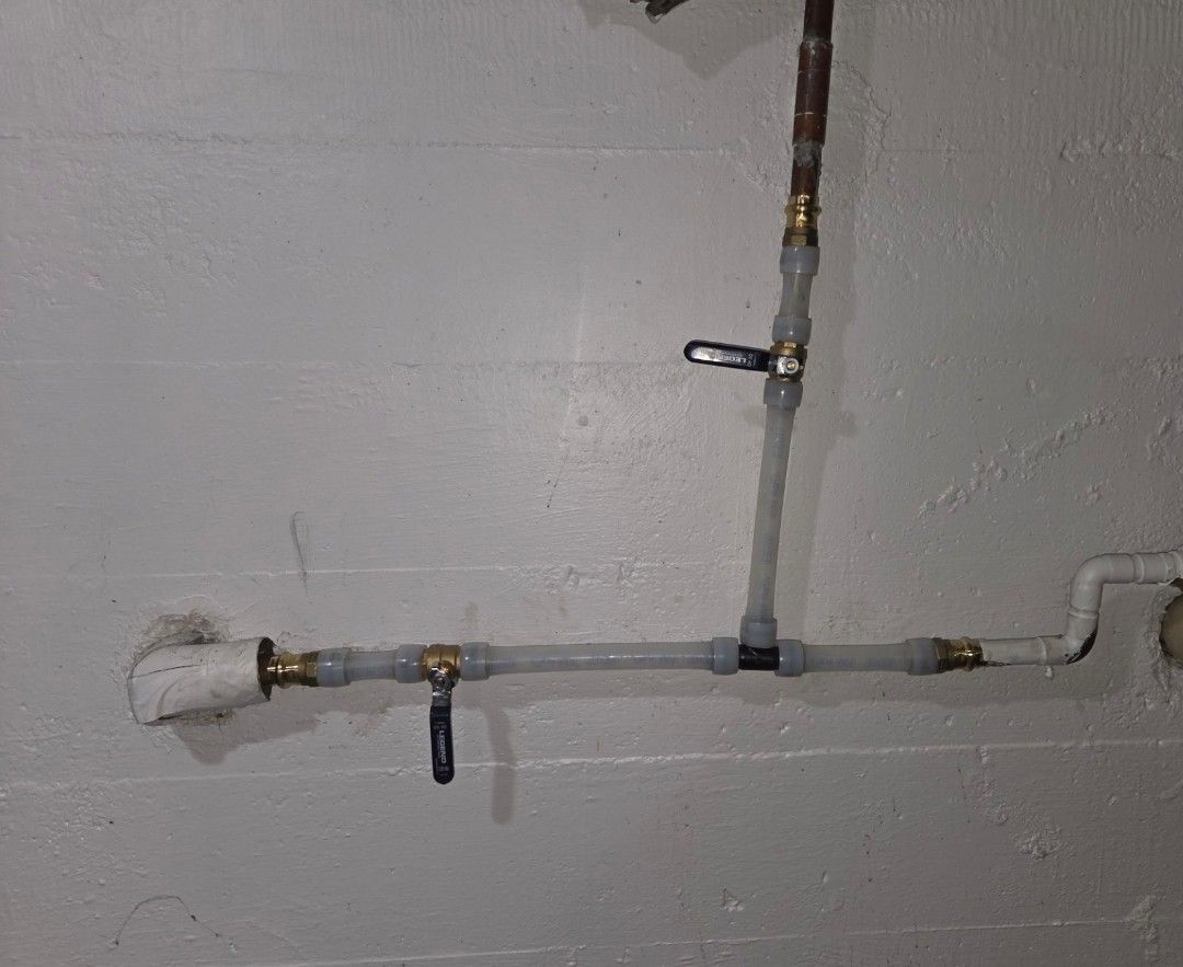 Wall-mounted plumbing pipes and valves in a basement or utility room, with white insulated pipe and gray concrete wall.
