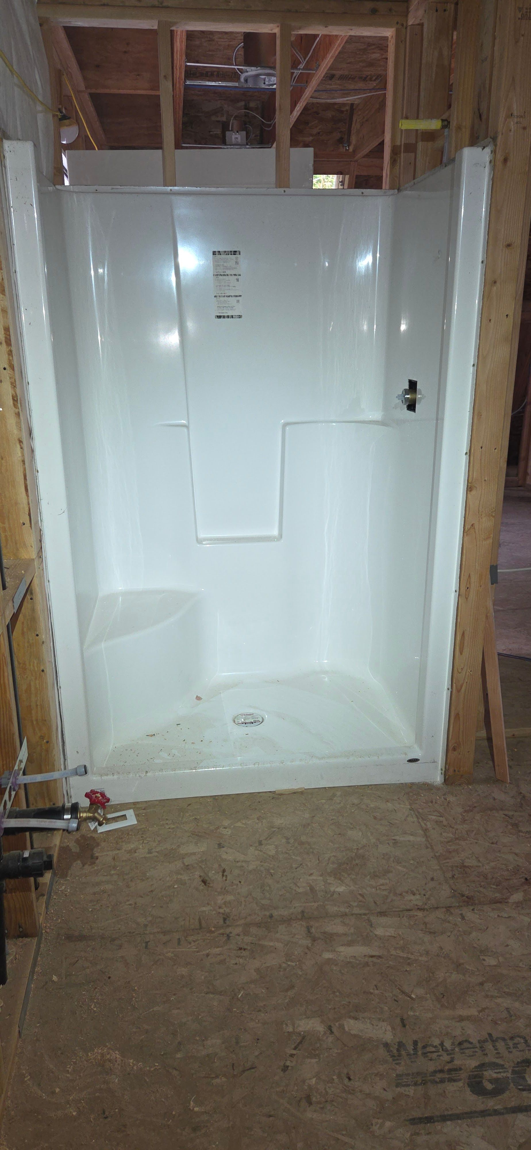A white fiberglass shower stall with a built-in seat, installed in a bathroom frame during construction.