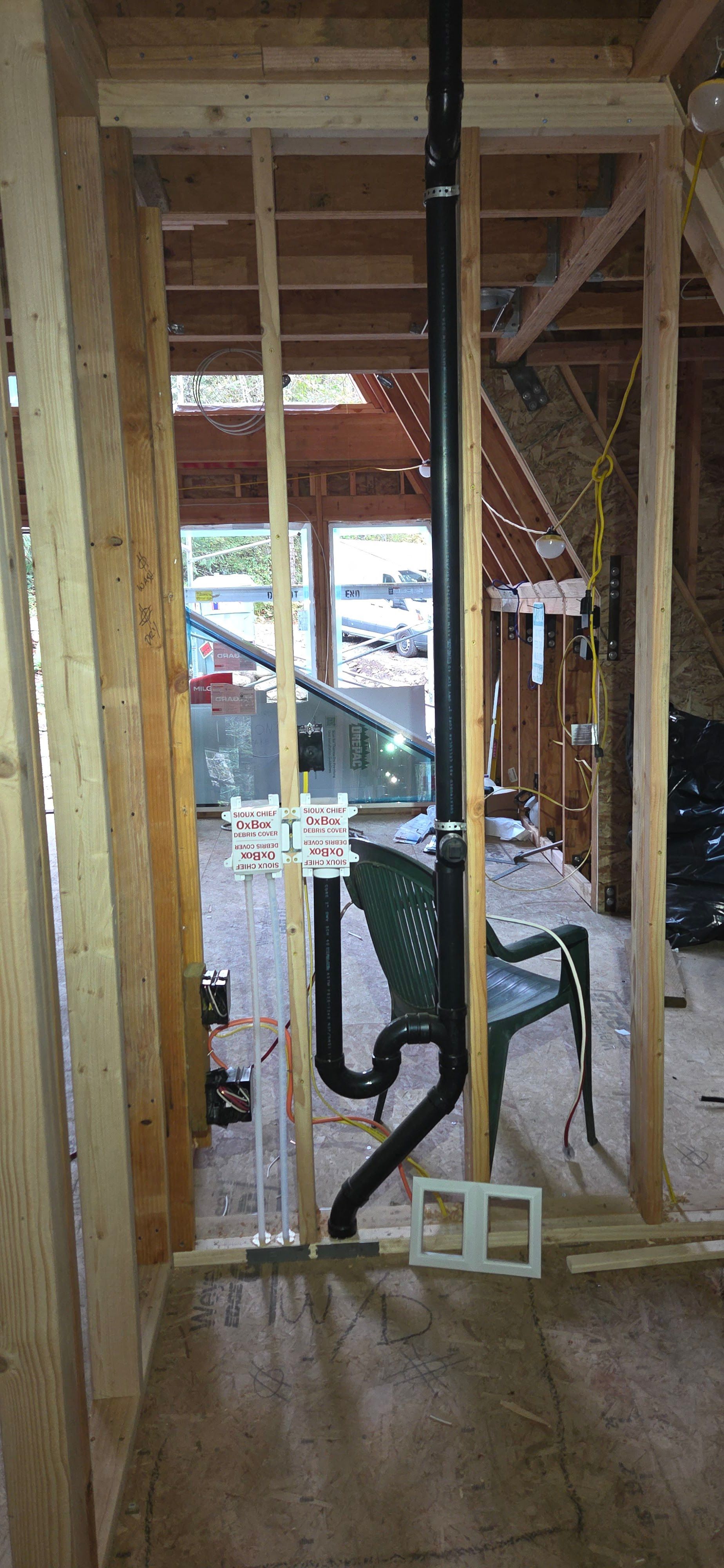 A vertical black plumbing pipe with a U-shaped p-trap assembly installed within unfinished wooden wall framing.