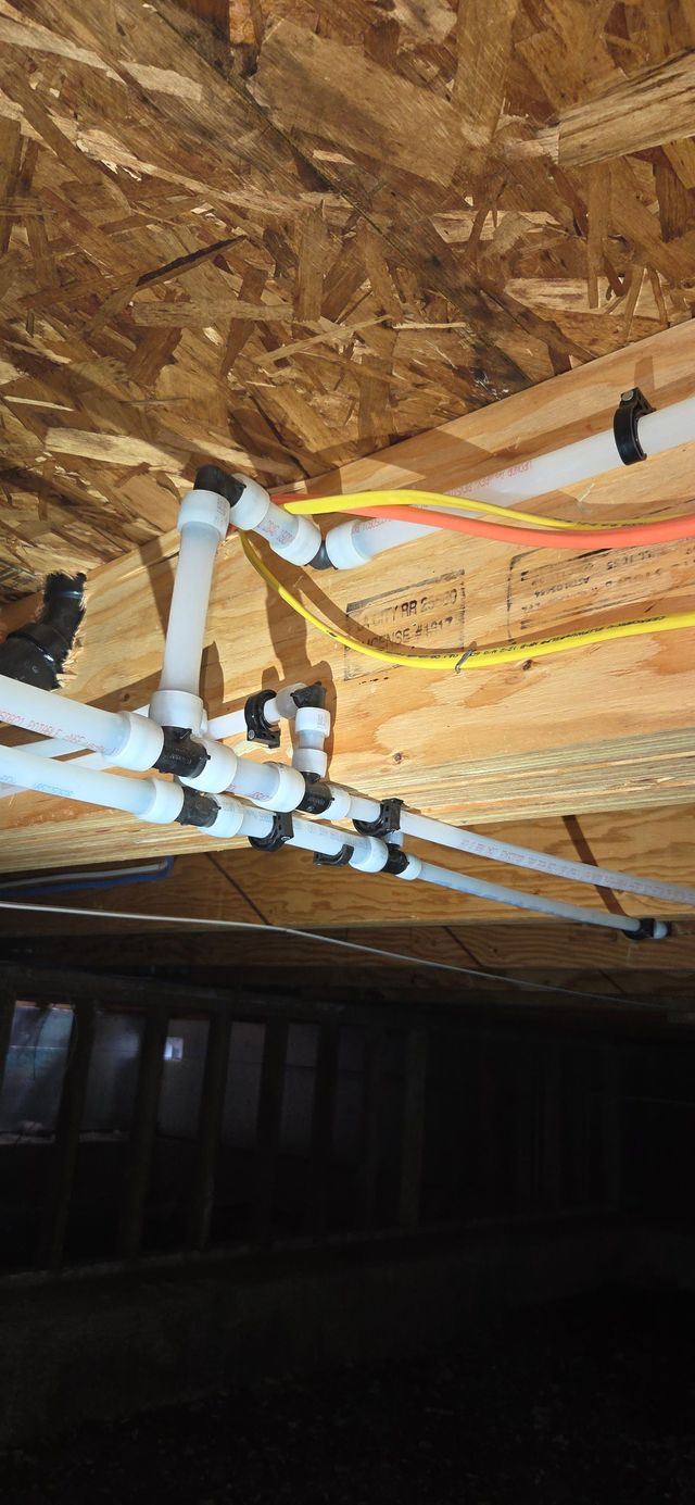 Plumbing pipes installed beneath a wood structure, with electrical wiring visible.