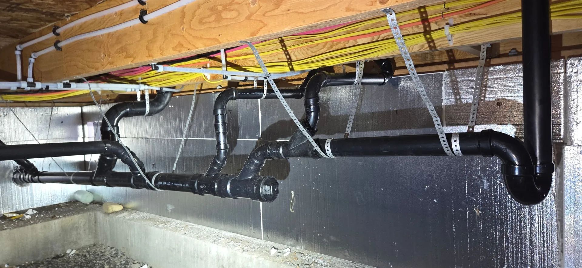Black and white pipes running beneath a wooden ceiling with visible water dripping below