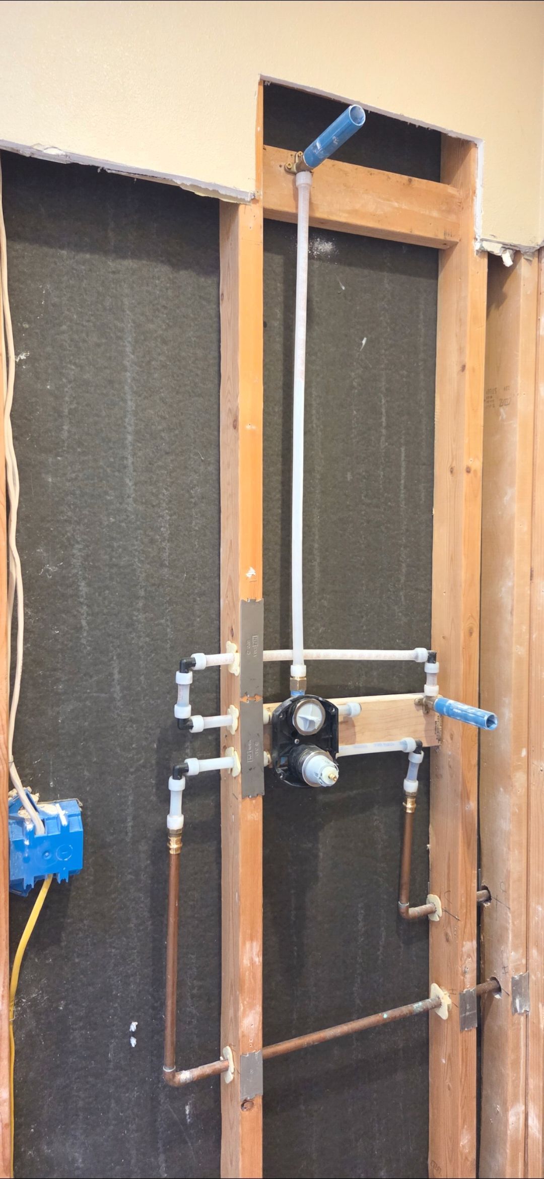 Plumbing pipes and a shower valve installed between wooden wall studs inside a home under renovation.