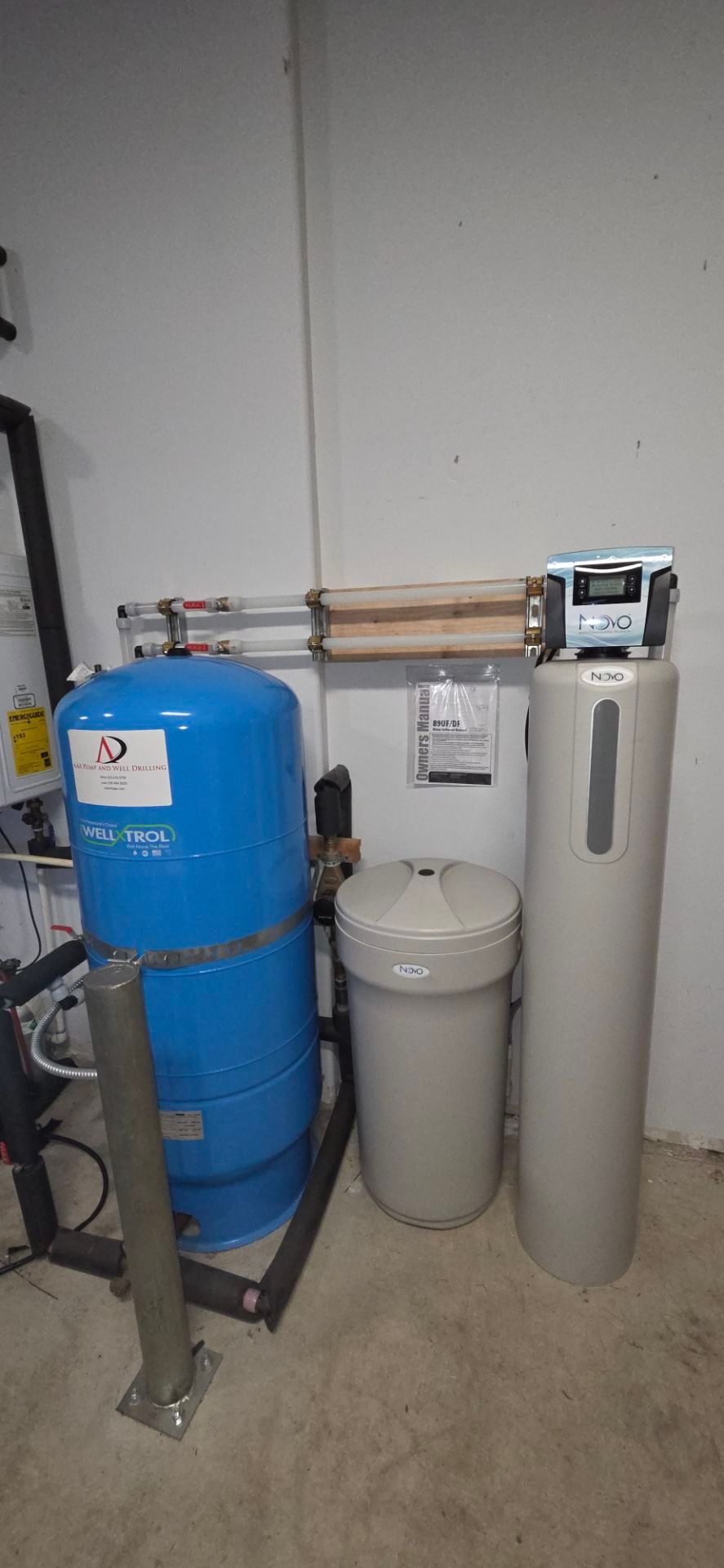 A blue water pressure tank and a beige water softening system with a brine tank standing on a concrete floor indoors.