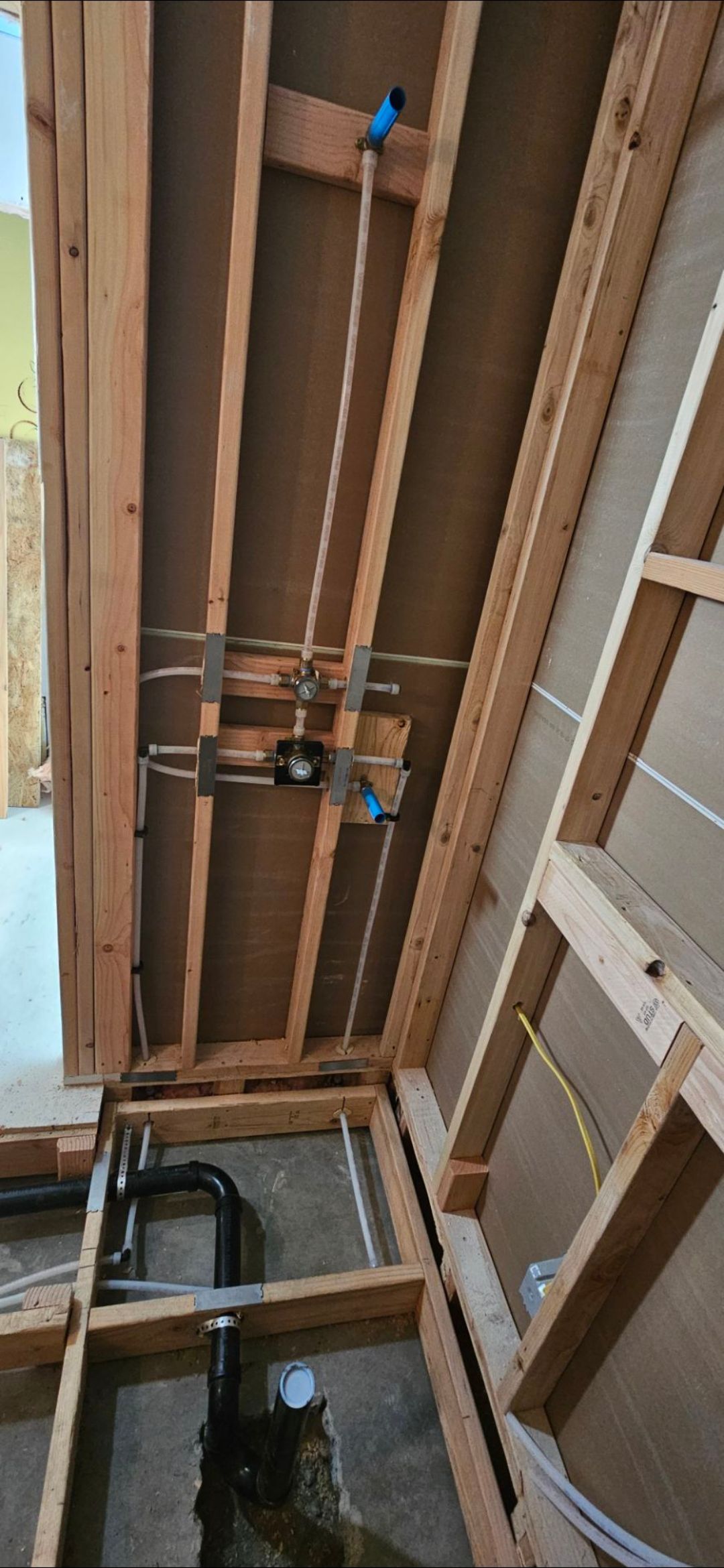 Plumbing installation for a shower showing internal PEX lines, a mixing valve, and a drain pipe within wooden wall studs.