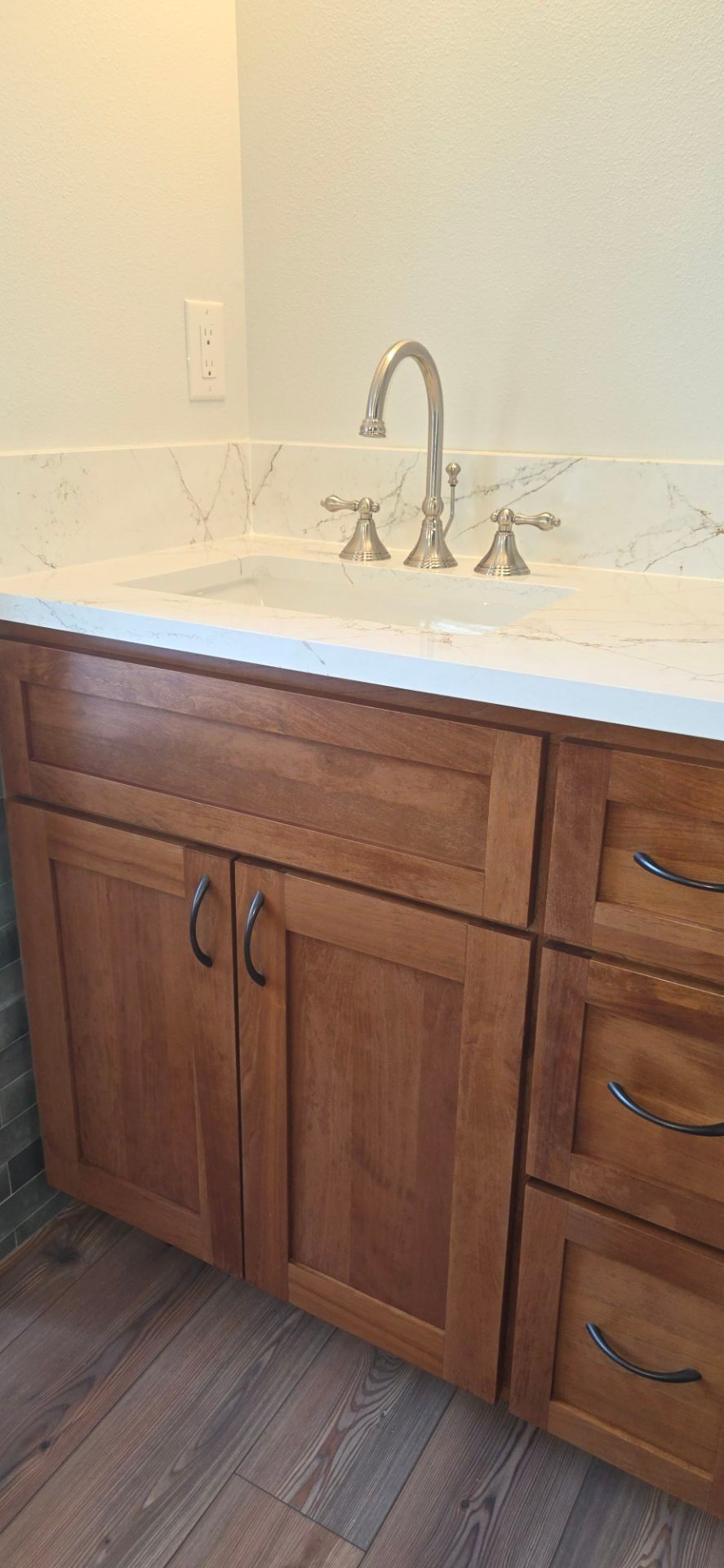 A bathroom vanity with a white countertop, silver faucet, wood cabinets, and drawers over wood-look flooring.