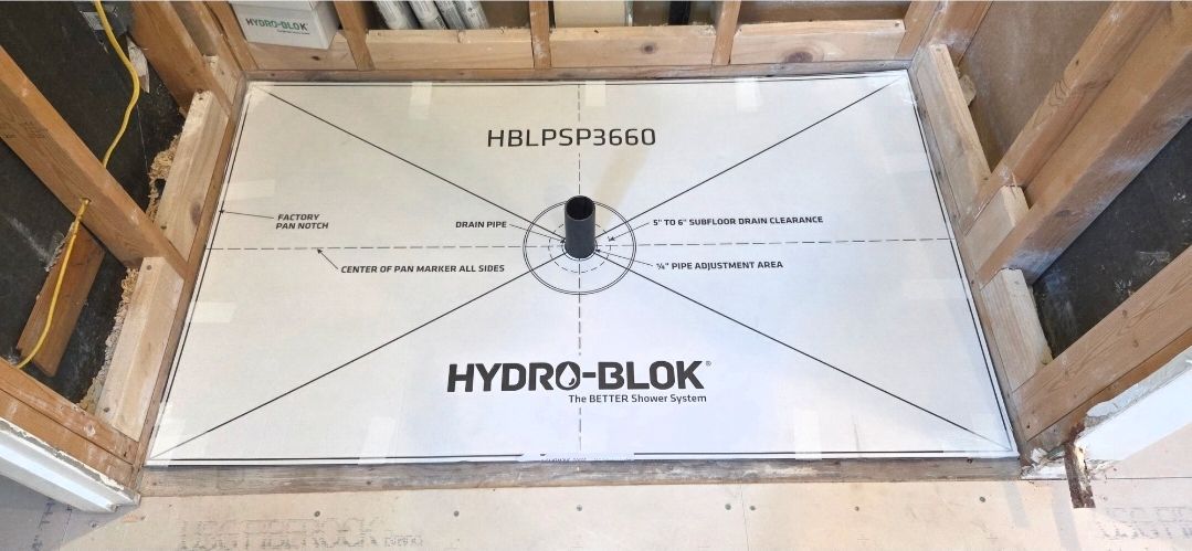 A white Hydro-Blok shower pan installed in a wooden stud frame with a central drain pipe protruding through the center.