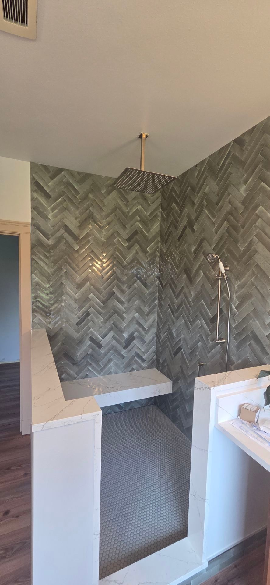 A walk-in shower with gray herringbone-patterned tile walls, a built-in bench, and a gold overhead showerhead.