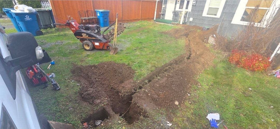 A trench dug in a residential lawn with a walk-behind trencher machine parked nearby on the grass.
