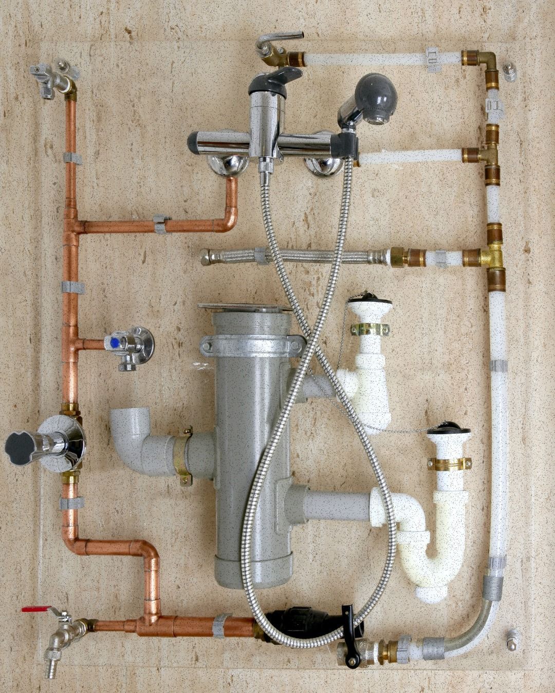 Plumbing display on a textured wall featuring copper pipes, a chrome shower mixer, grey drainage pipes, and white P-traps.