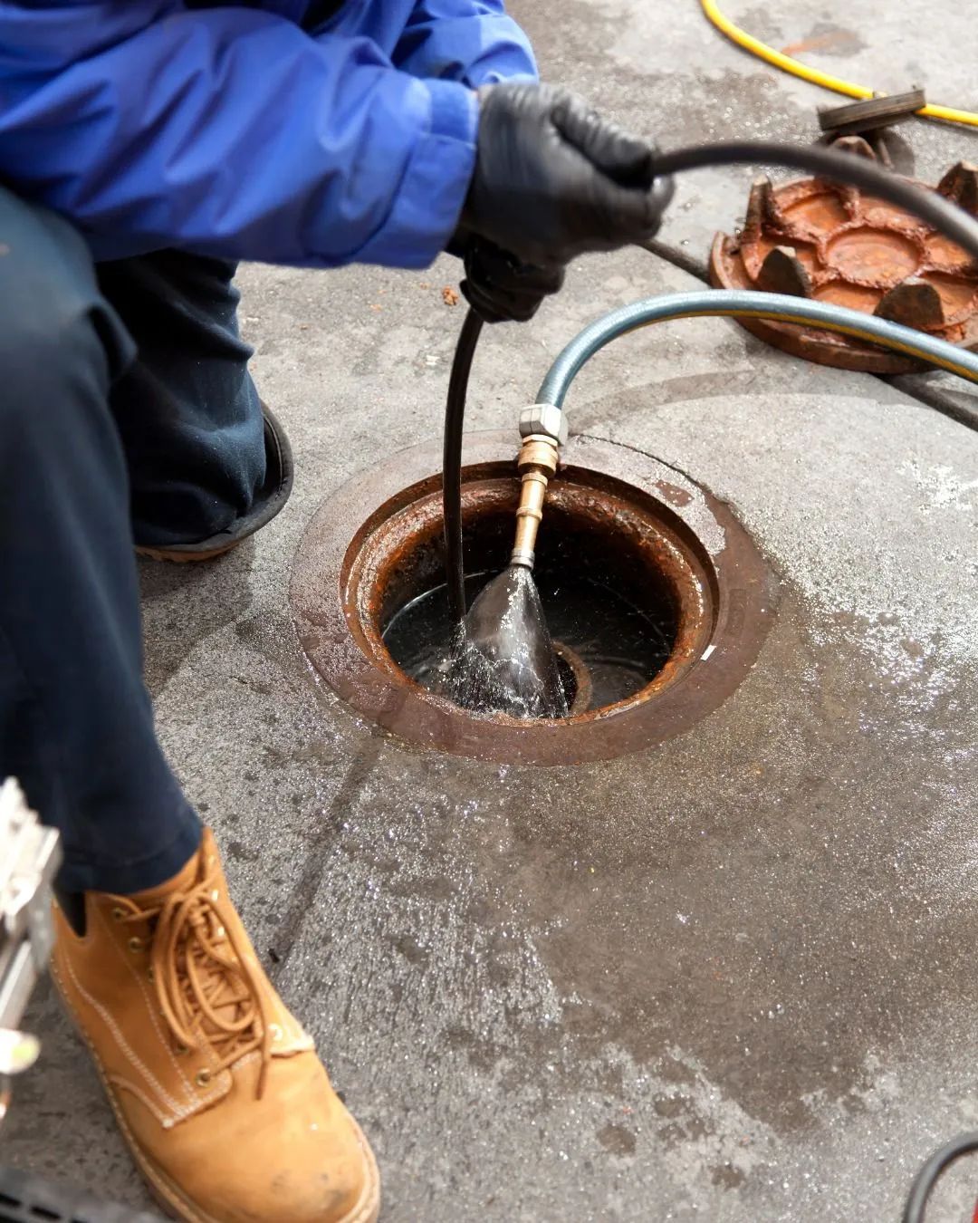 Worker using a hose to clean a manhole in a concrete pavement.