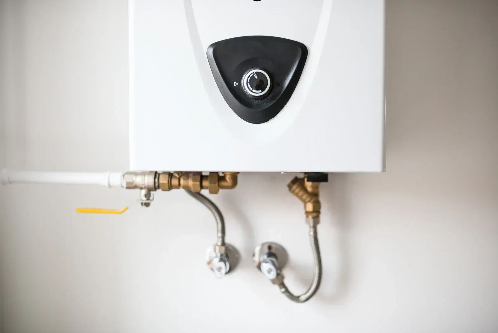 White wall-mounted water heater with pipes and valves.