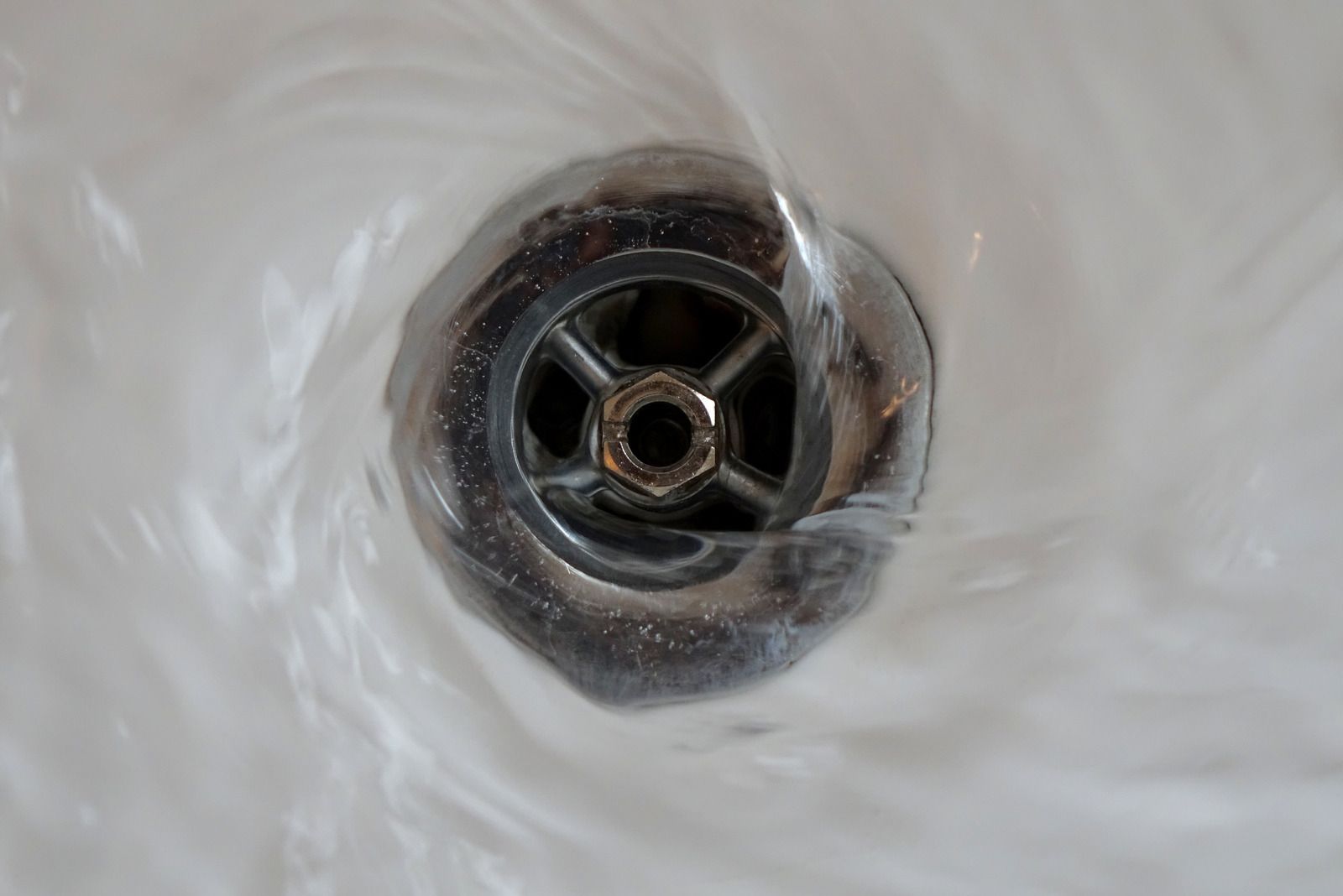 Close-up of a sink drain with a metal strainer surrounded by water droplets