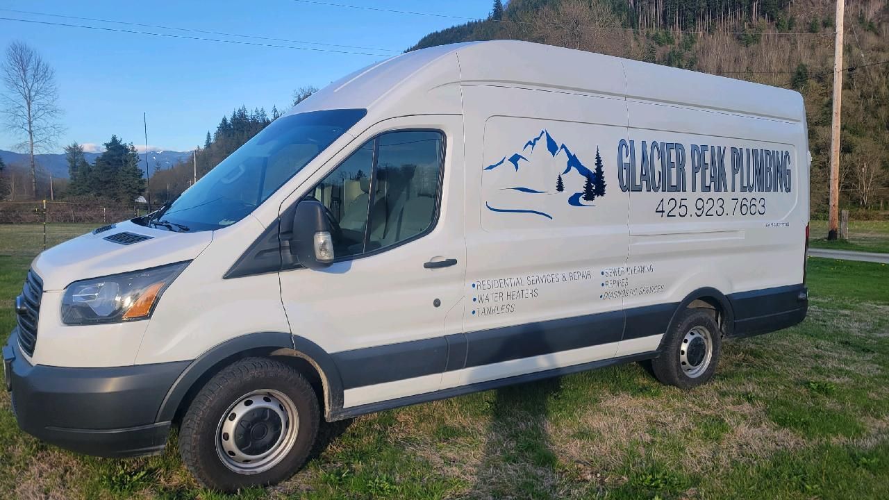 A white Glacier Peak Plumbing work van parked on grass, with a mountain logo and phone number on its side.