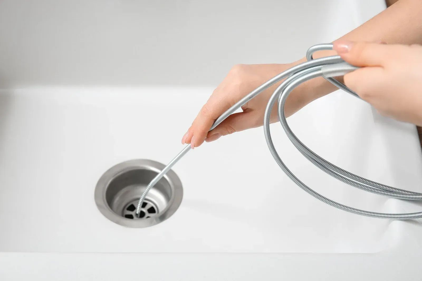 Hand inserting a silver drain snake into a white sink drain