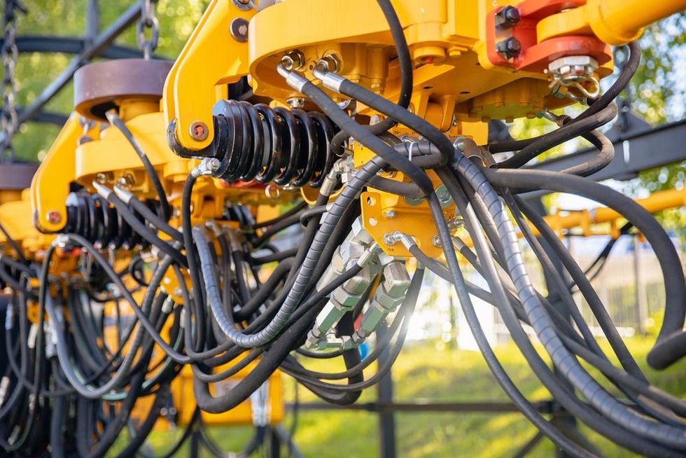 Close-up of yellow agricultural machinery with tangled black hoses in a field