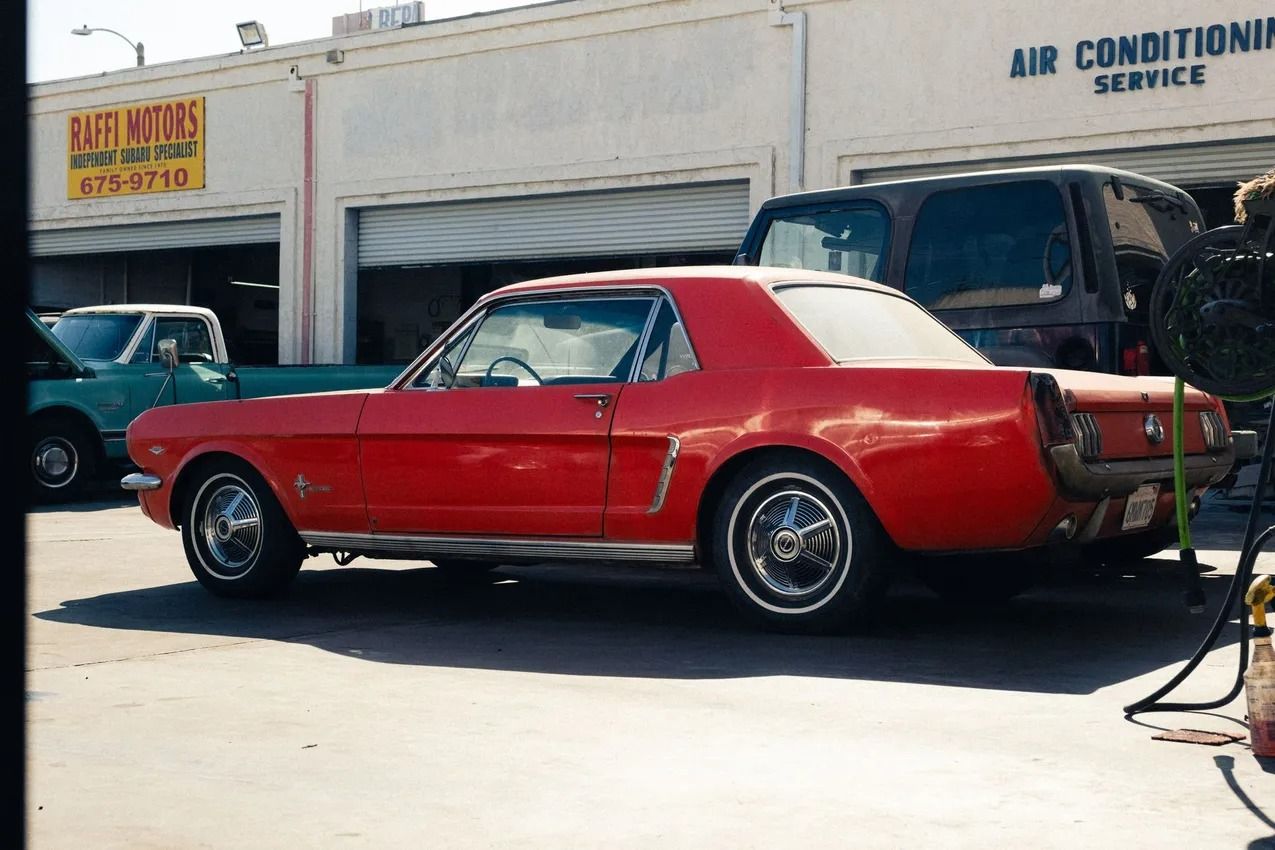 Red classic car parked outside an auto service garage with an air conditioning sign. | Bob's Auto Repair