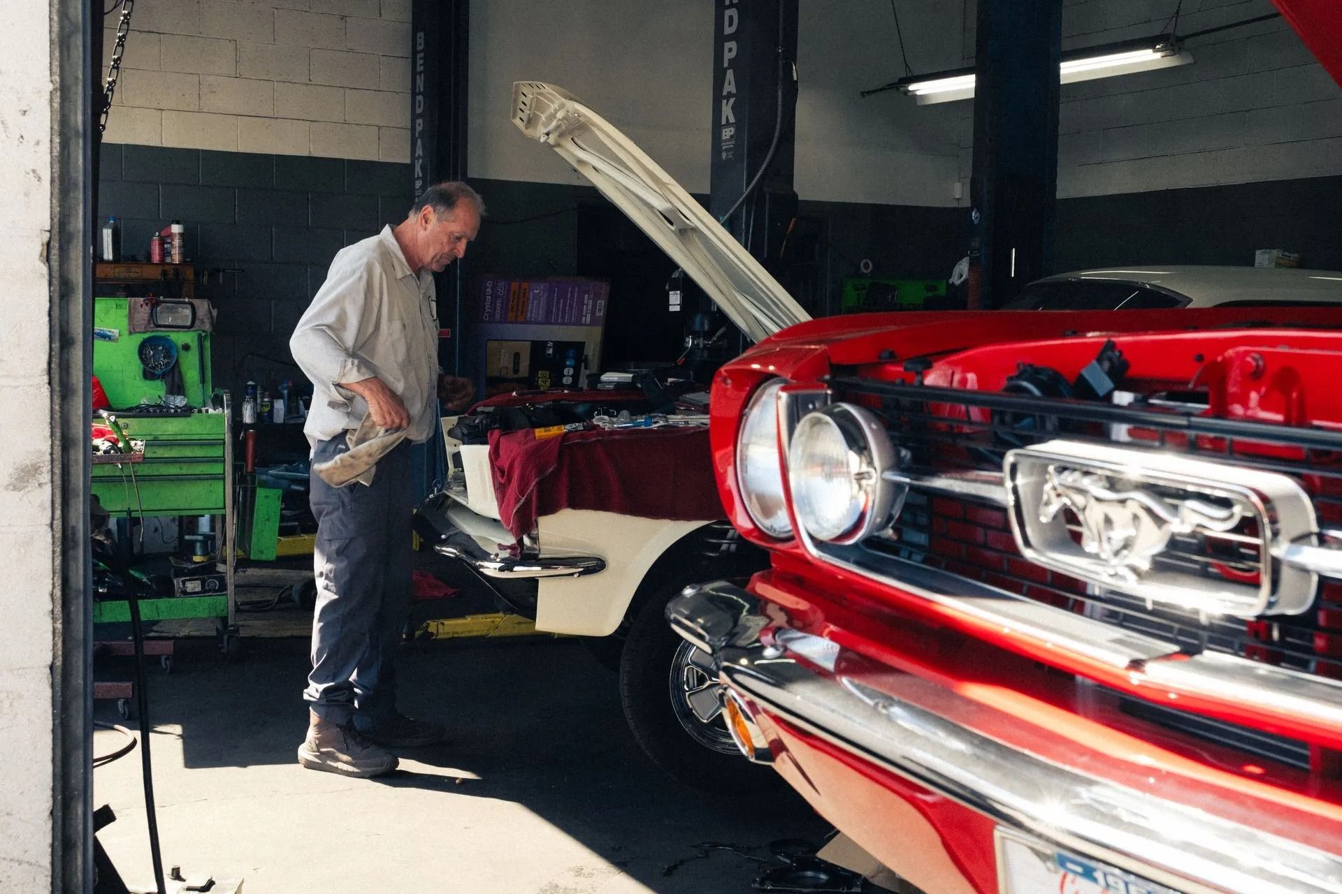 Mechanic working beside a red classic car with hood open in a garage | Bob's Auto Repair