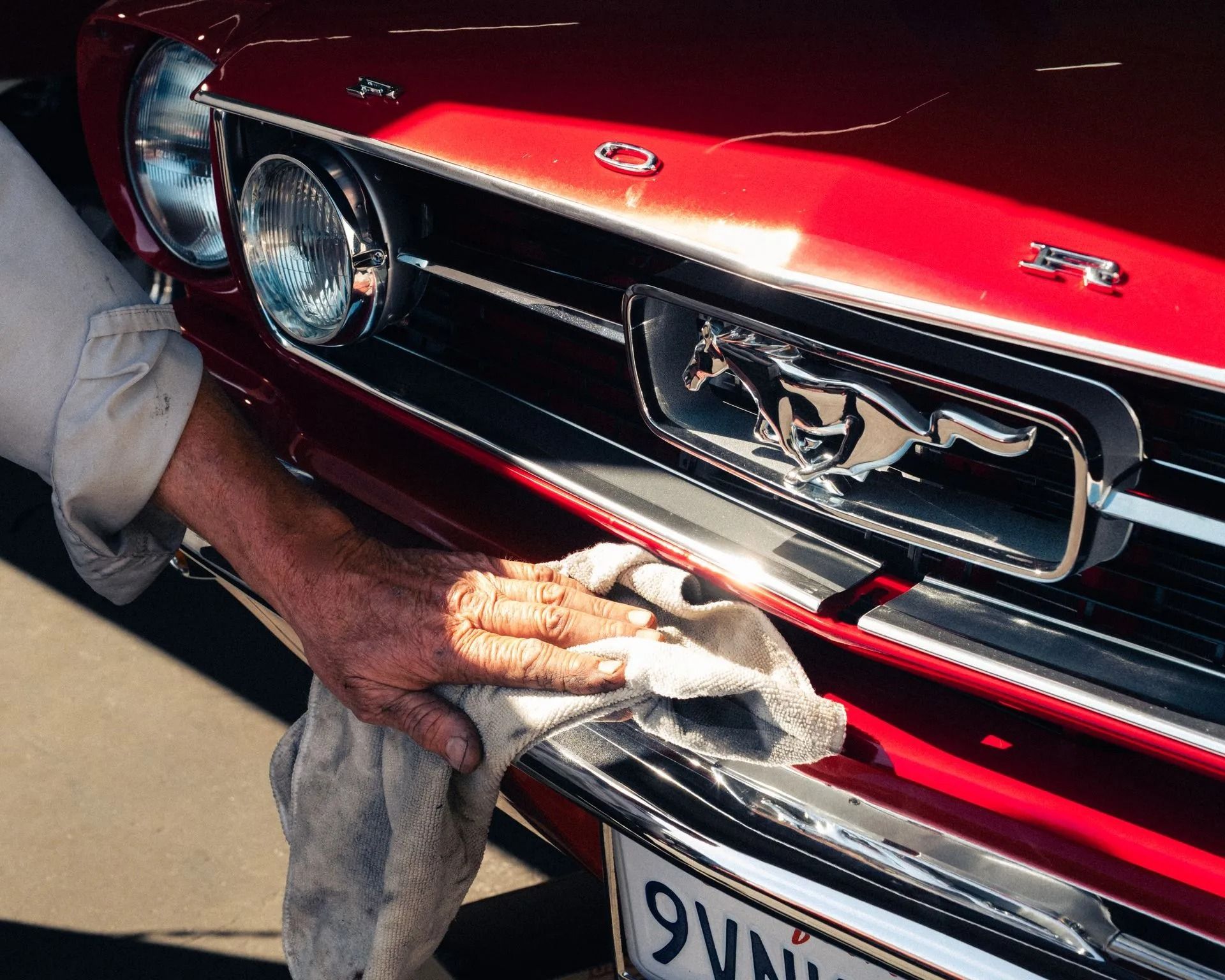 Hand polishing the chrome grille of a red Ford Mustang with a cloth | Bob's Auto Repair