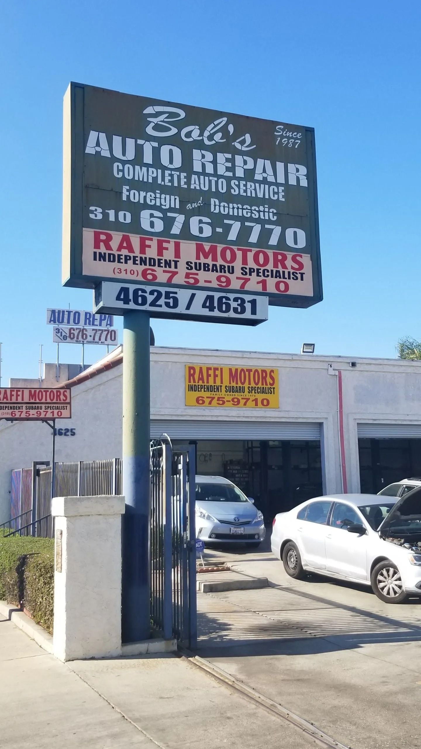 Auto repair shop with large sign, parked cars, and a gated entrance on a sunny street. | Bob's Auto Repair