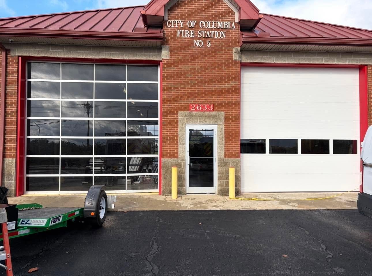 Brick fire station exterior with a red roof, large garage doors, and a glass entrance door