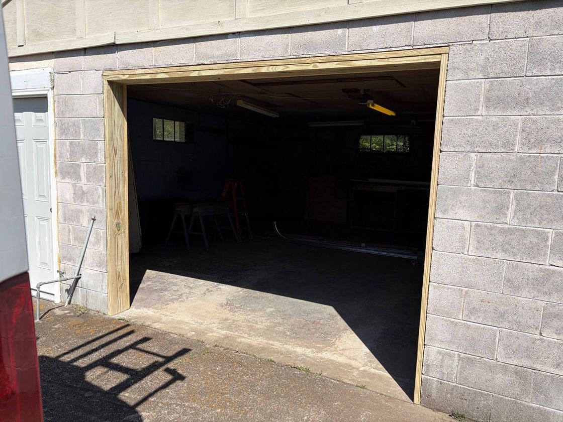Open garage with concrete block walls and a shadowed interior, seen from outside in daylight