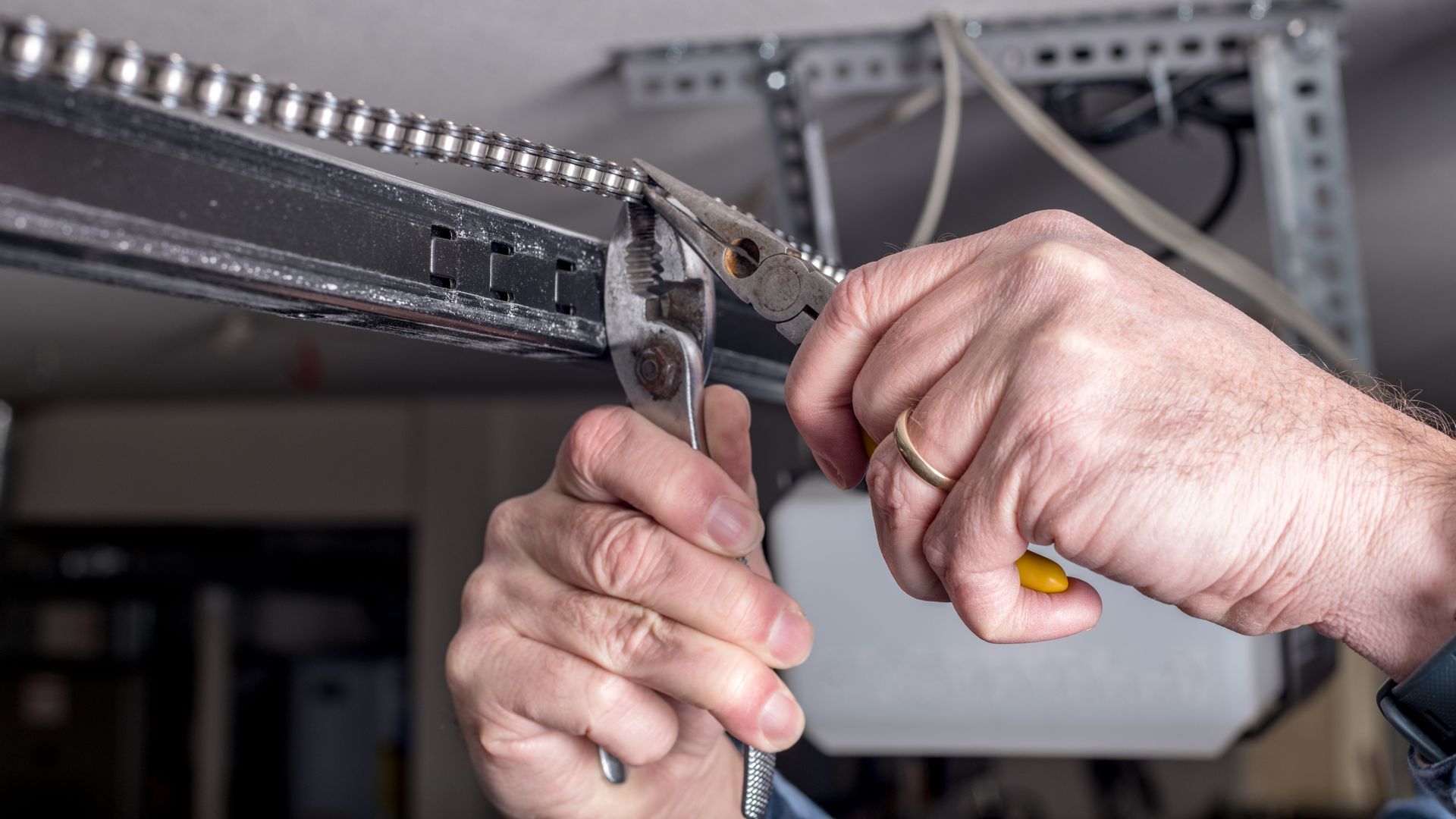 Hands using pliers to cut a metal chain on a garage door track.