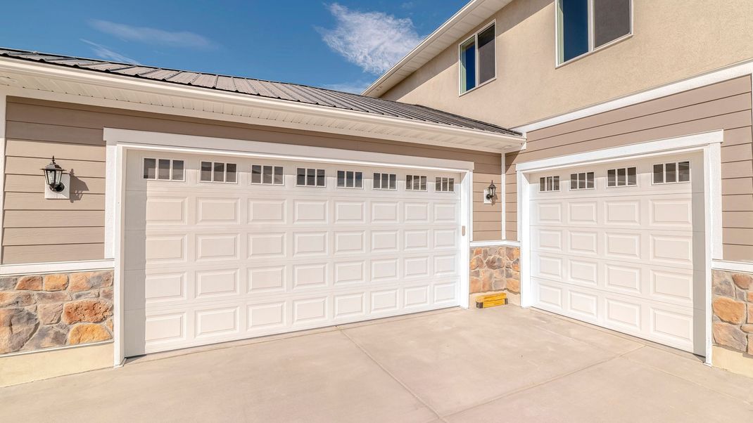Two white garage doors on a beige stucco house under a bright blue sky