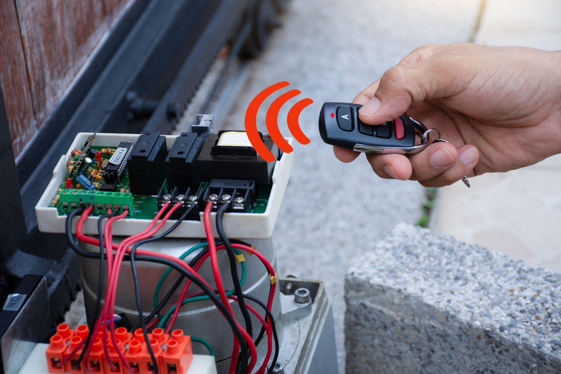 Hand holding a remote control beside an open electrical control box with wires and circuit boards