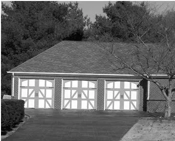 Three-car garage with white doors and a gray shingled roof, viewed from the driveway