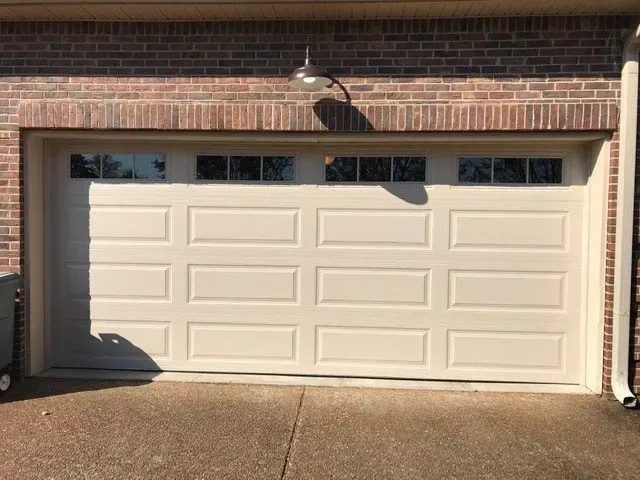 White double garage door on a brick house, lit by a wall-mounted light.