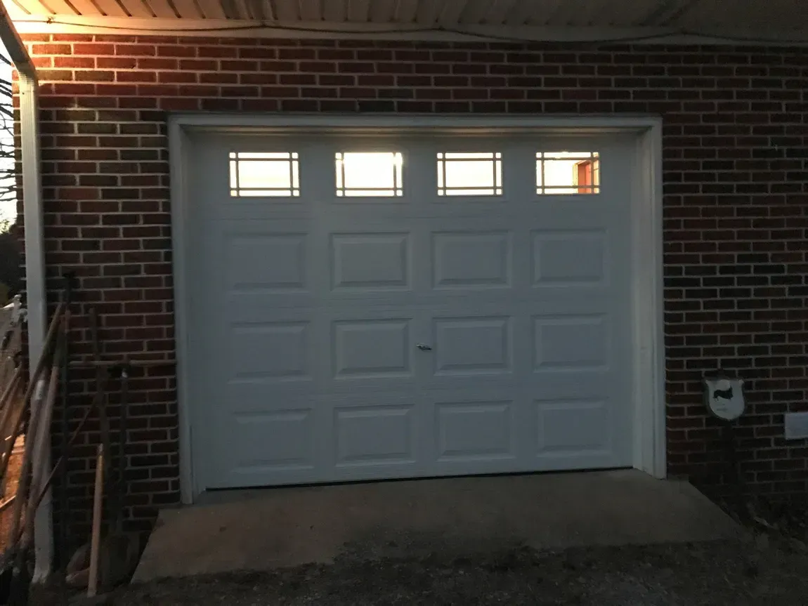 White garage door in a brick building with three small windows and a sloped concrete driveway