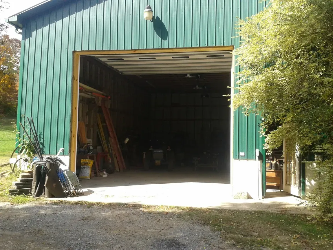 Green metal garage with an open doorway, bright sunlight, and tools visible inside