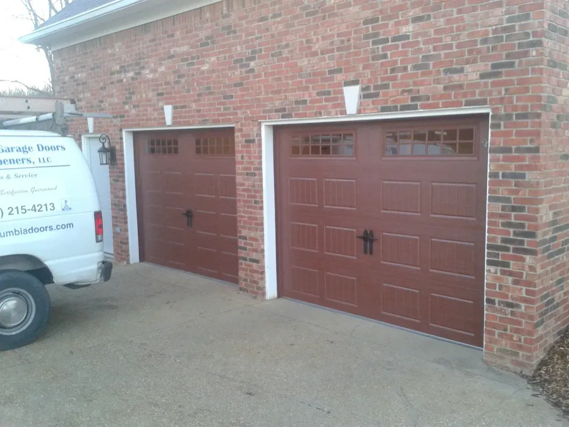 Brick garage with two brown doors beside a white van on a driveway